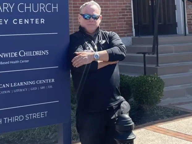 Dr Leve leaning against a wayfinding sign outside a church and learning centre on Third Street.